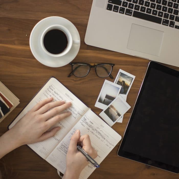 writing in journal with laptop and glasses